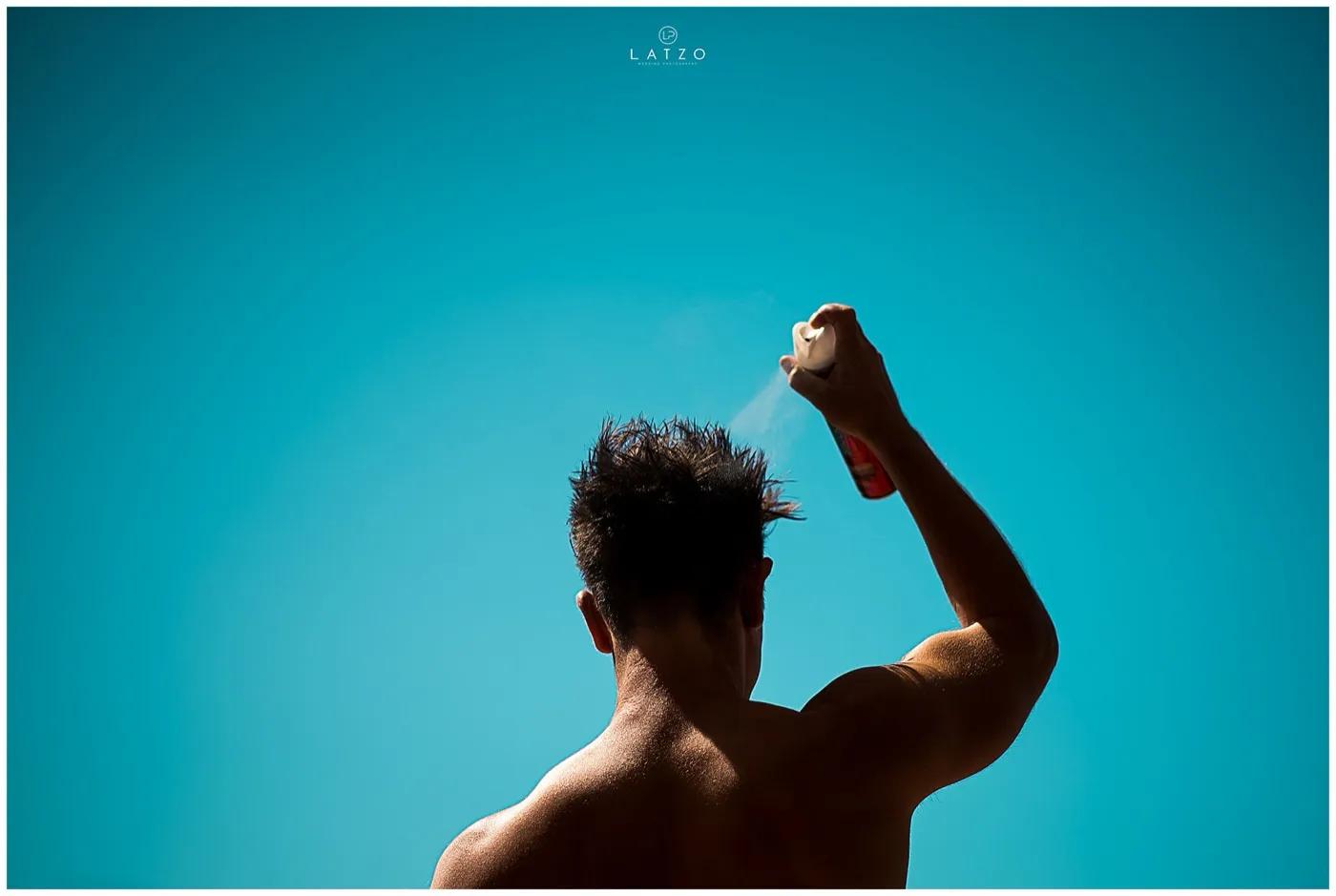 A shirtless man seen from behind sprays his spiky hair against a bright turquoise sky.