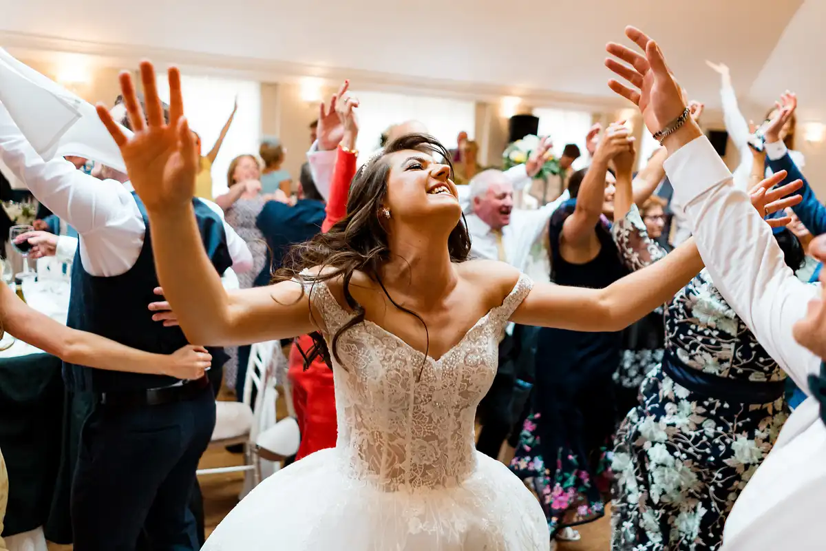 Bride dancing with her arms out and eyes half closed, guests behind her with hands in the air.