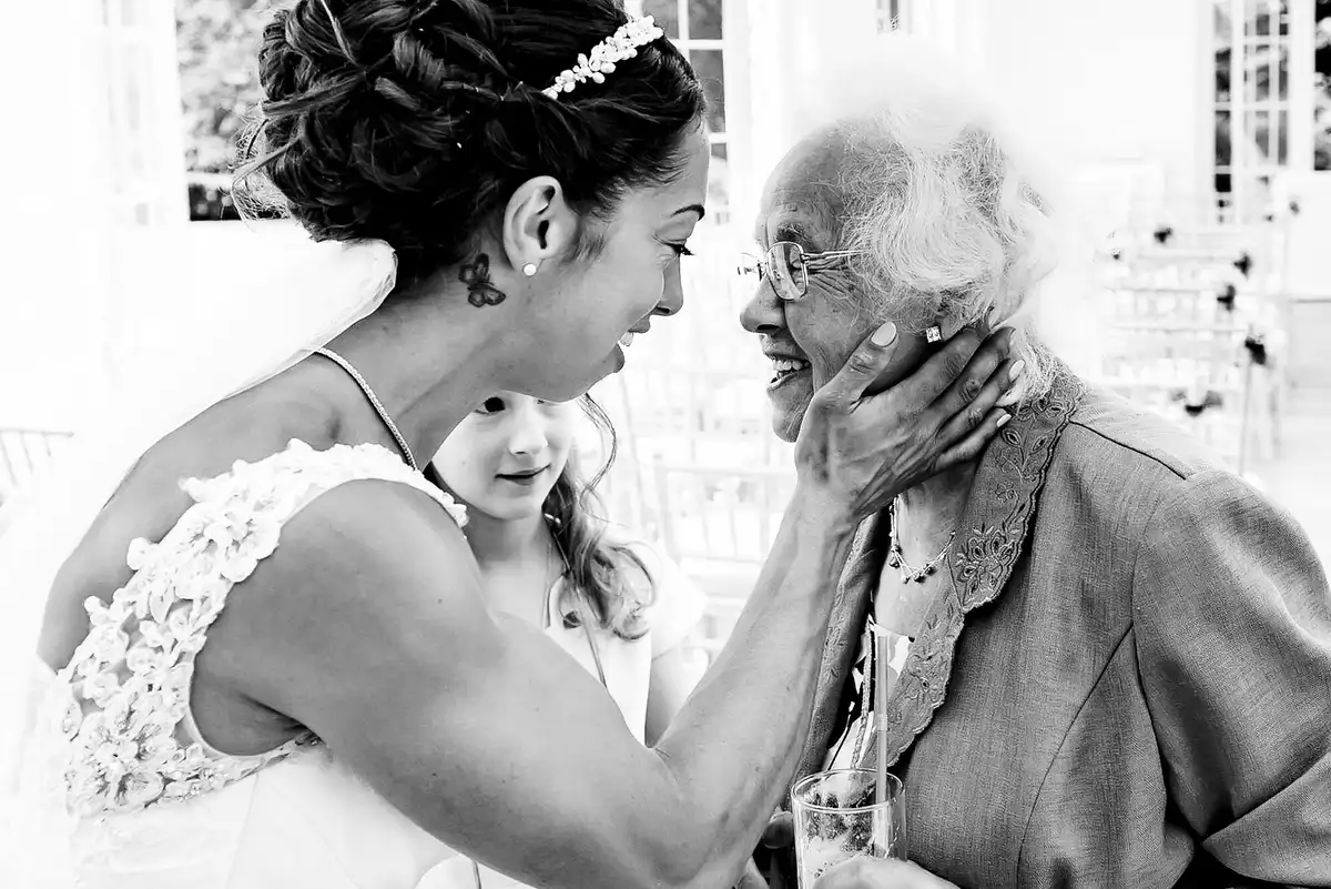 Black and white of the bride cupping an older woman's face as a young girl peeks between them.