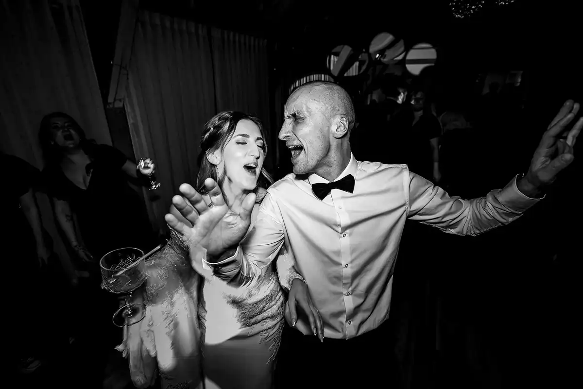 Black and white of the bride and a man in a bow tie singing loudly together on the dance floor.