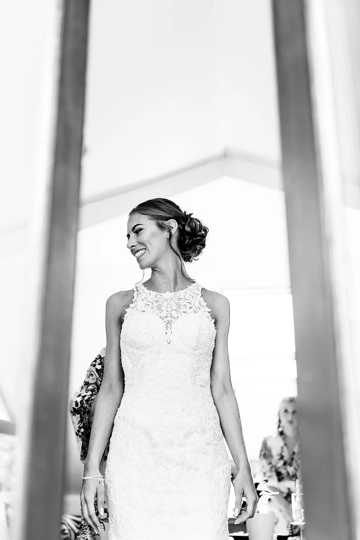 Black and white of the bride in a lace halter dress smiling over her shoulder in a bright marquee doorway.