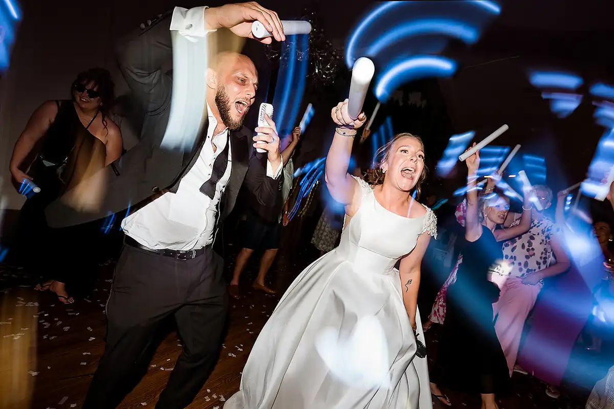 Bride and groom dance wildly with glow sticks, blue light trails swirling round the guests.
