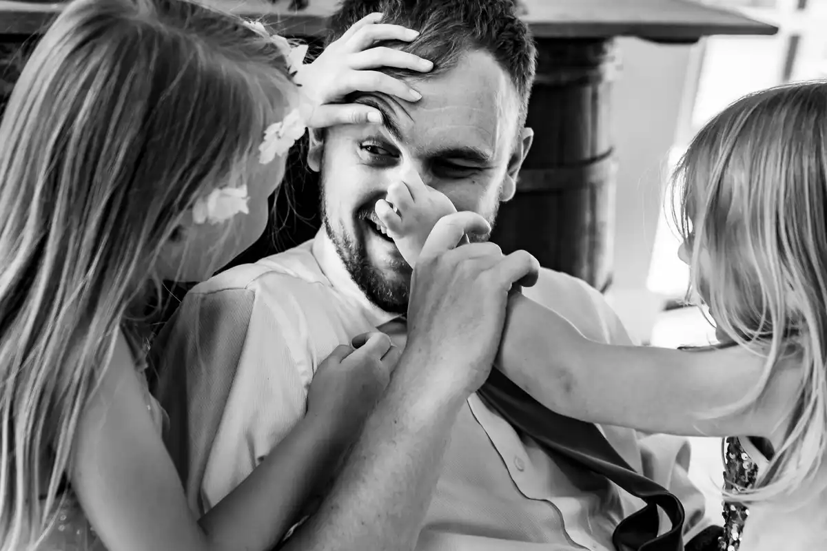 Black and white of two young girls squishing a smiling man's face and pushing his nose.