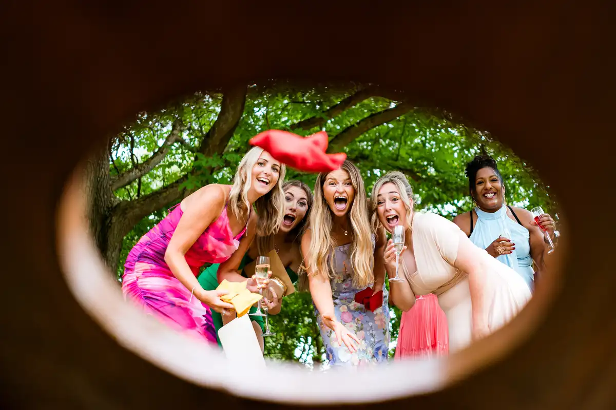 Guests seen through a cornhole board as a red beanbag flies towards the hole, all of them shrieking.