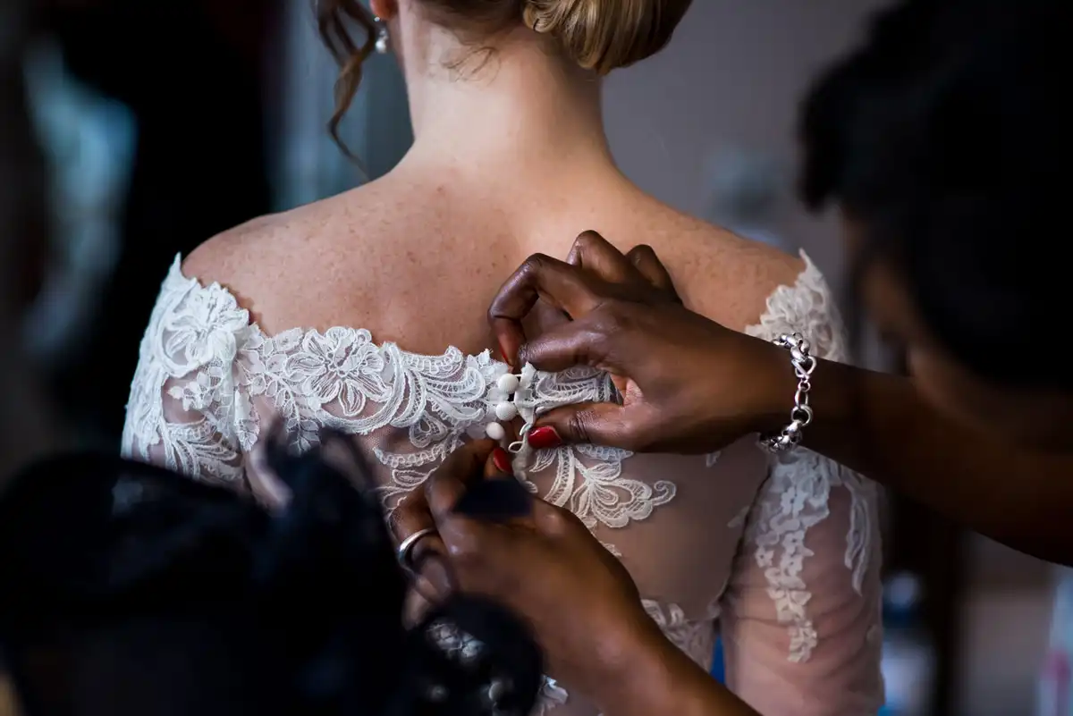 Close-up of hands fastening the row of buttons down the back of a bride's lace dress.