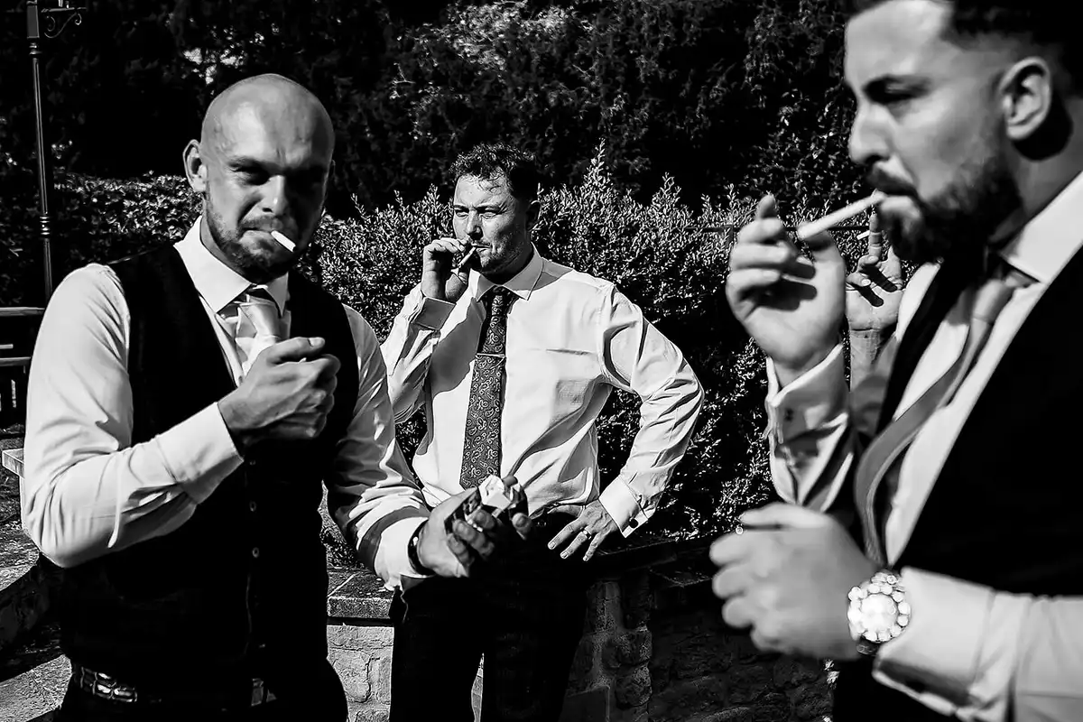 Black and white of three men in shirtsleeves and ties smoking in a garden.