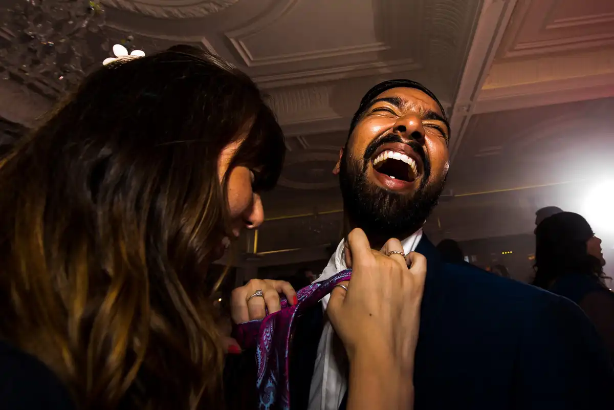 Man throws his head back laughing as a woman tugs at his tie at the reception.