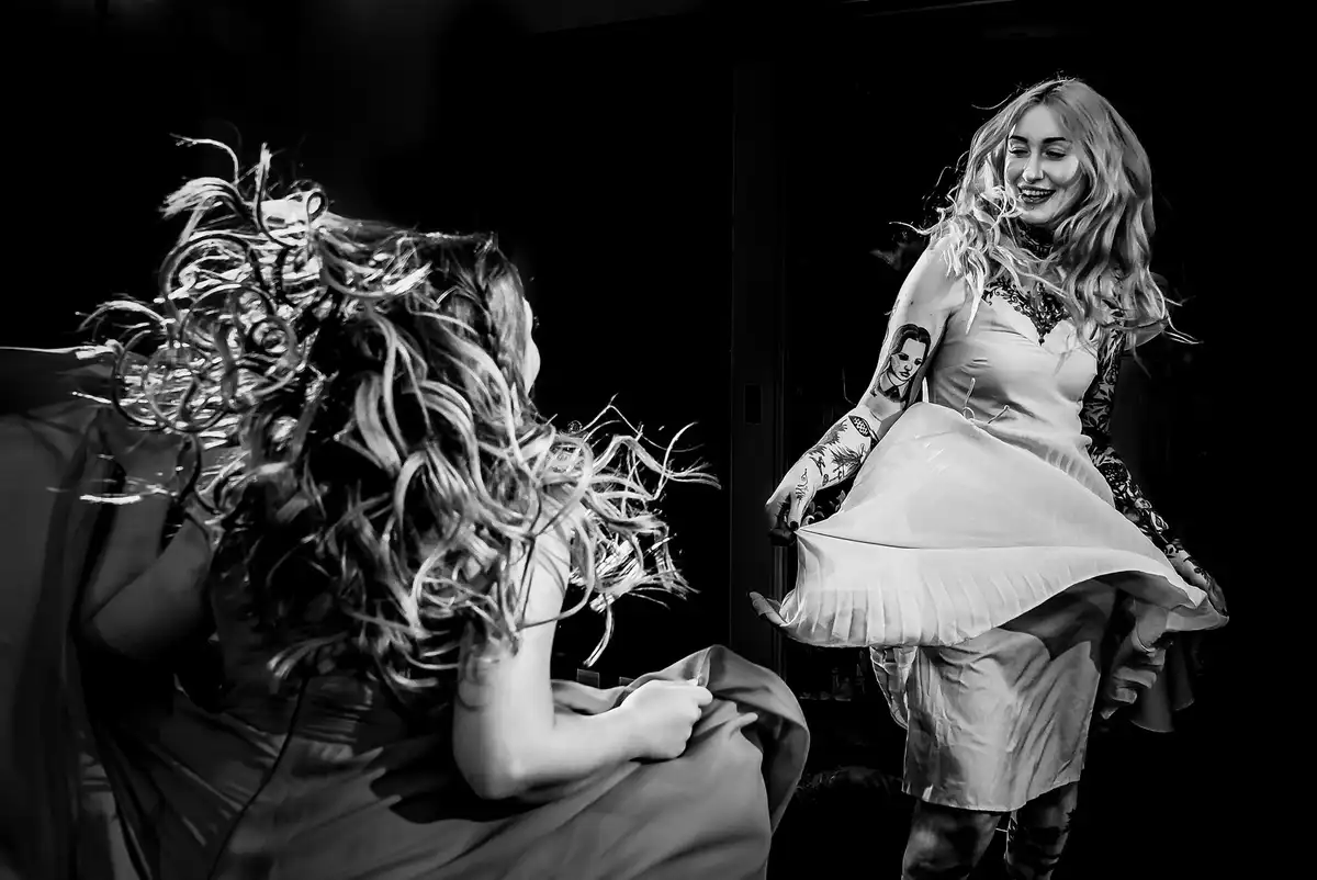 Black and white of two women dancing, long hair flying and skirts swishing against a dark background.