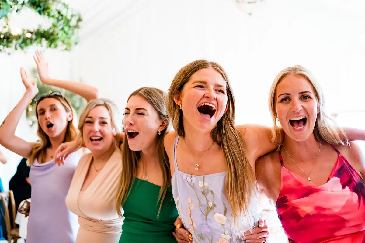 Five women arm in arm, singing at the tops of their voices at the reception.